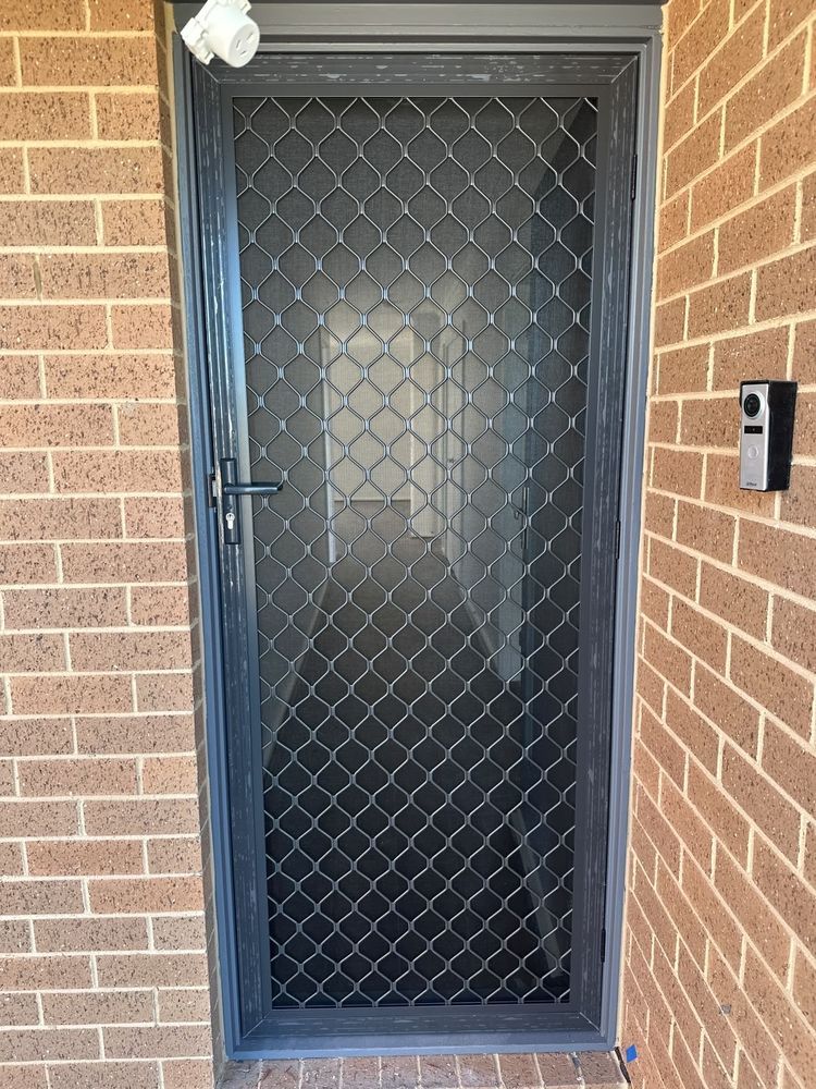 Grey aluminium security screen door with diamond mesh, installed on brick entryway